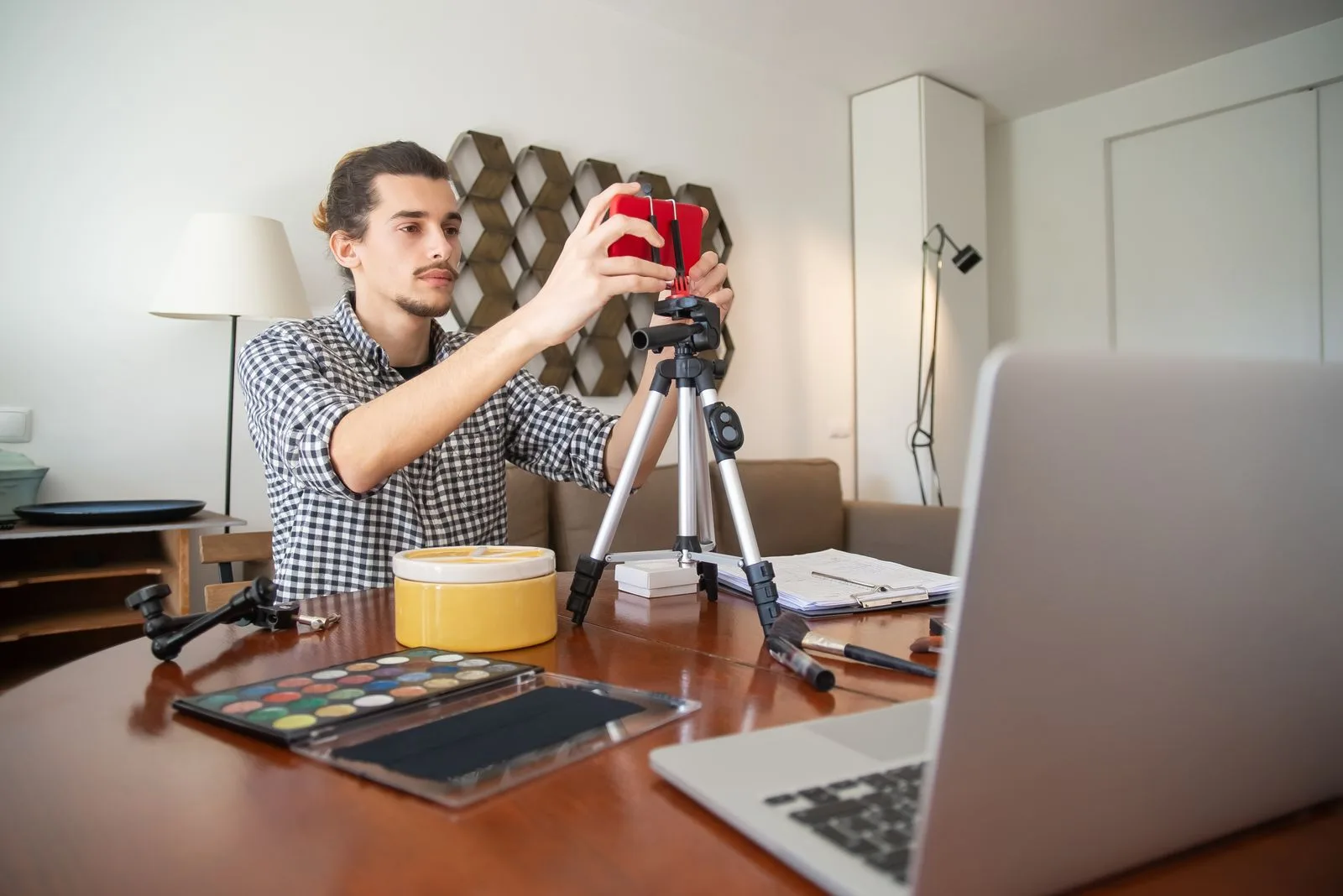 A male vlogger adjusts his camera on a tripod, preparing for a video shoot in a stylish home studio.